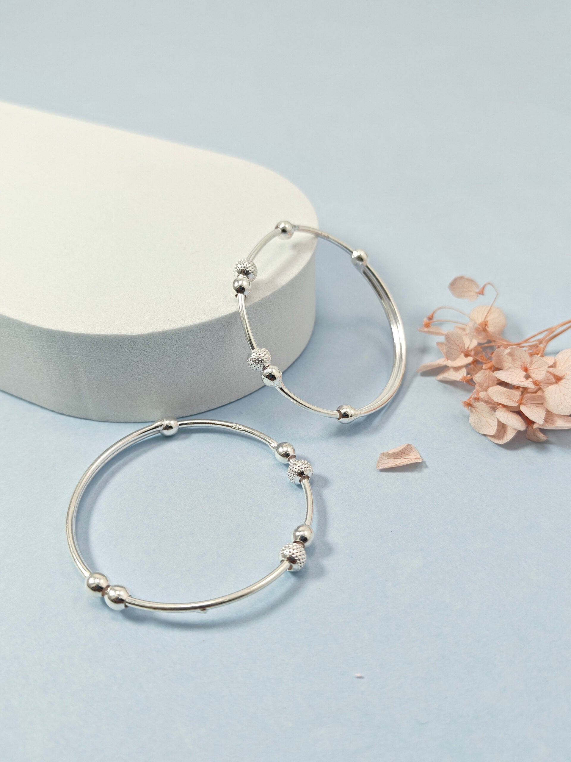 Silver hoop earrings on a light blue background with dried flowers.